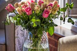 Photo shows vase of pink roses on table next to armchair