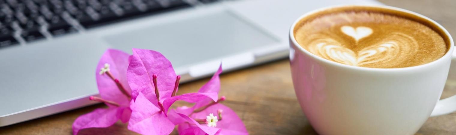 Flower next to a latte with a foam-decorated heart and a laptop