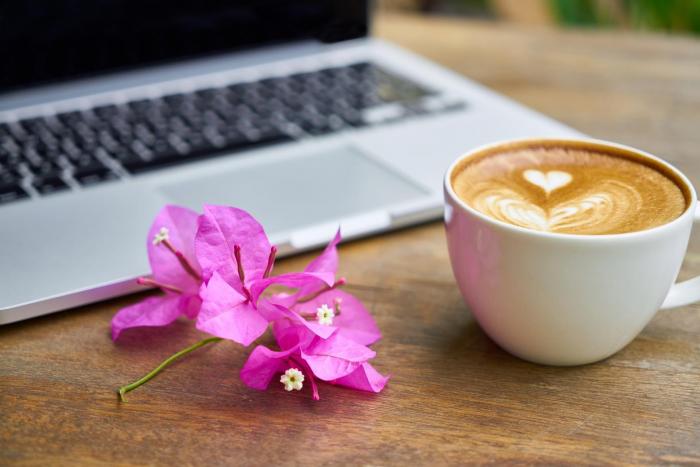 Flower next to a latte with a foam-decorated heart and a laptop
