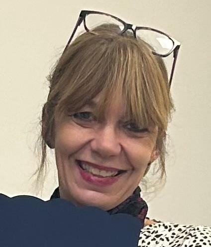 Photo shows Gina who wears her glasses on her head, has big smile and wearing black top