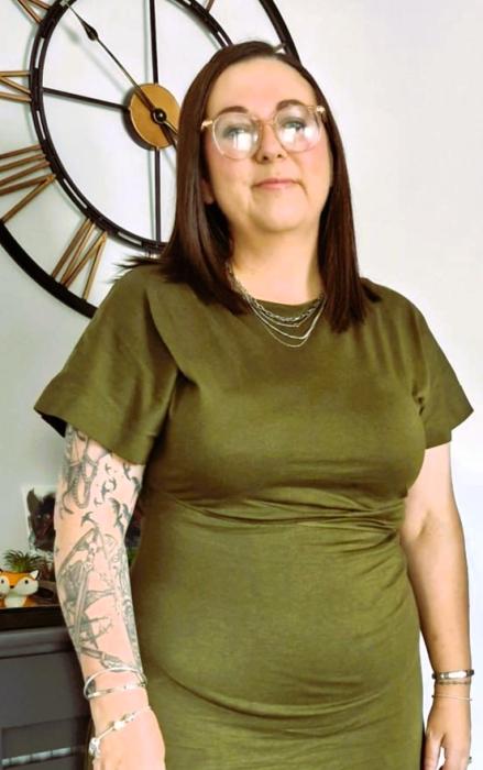 Photo shows manager standing in olive green dress, shoulder length hair & glasses