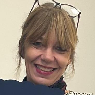 Photo shows Gina who wears her glasses on her head, has big smile and wearing black top