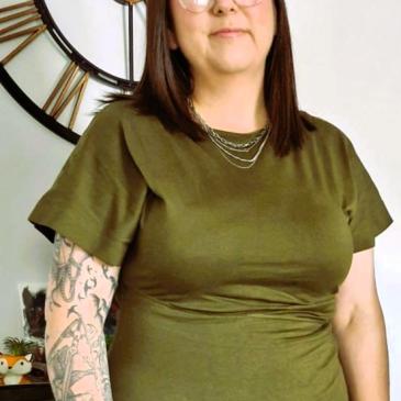 Photo shows manager standing in olive green dress, shoulder length hair & glasses